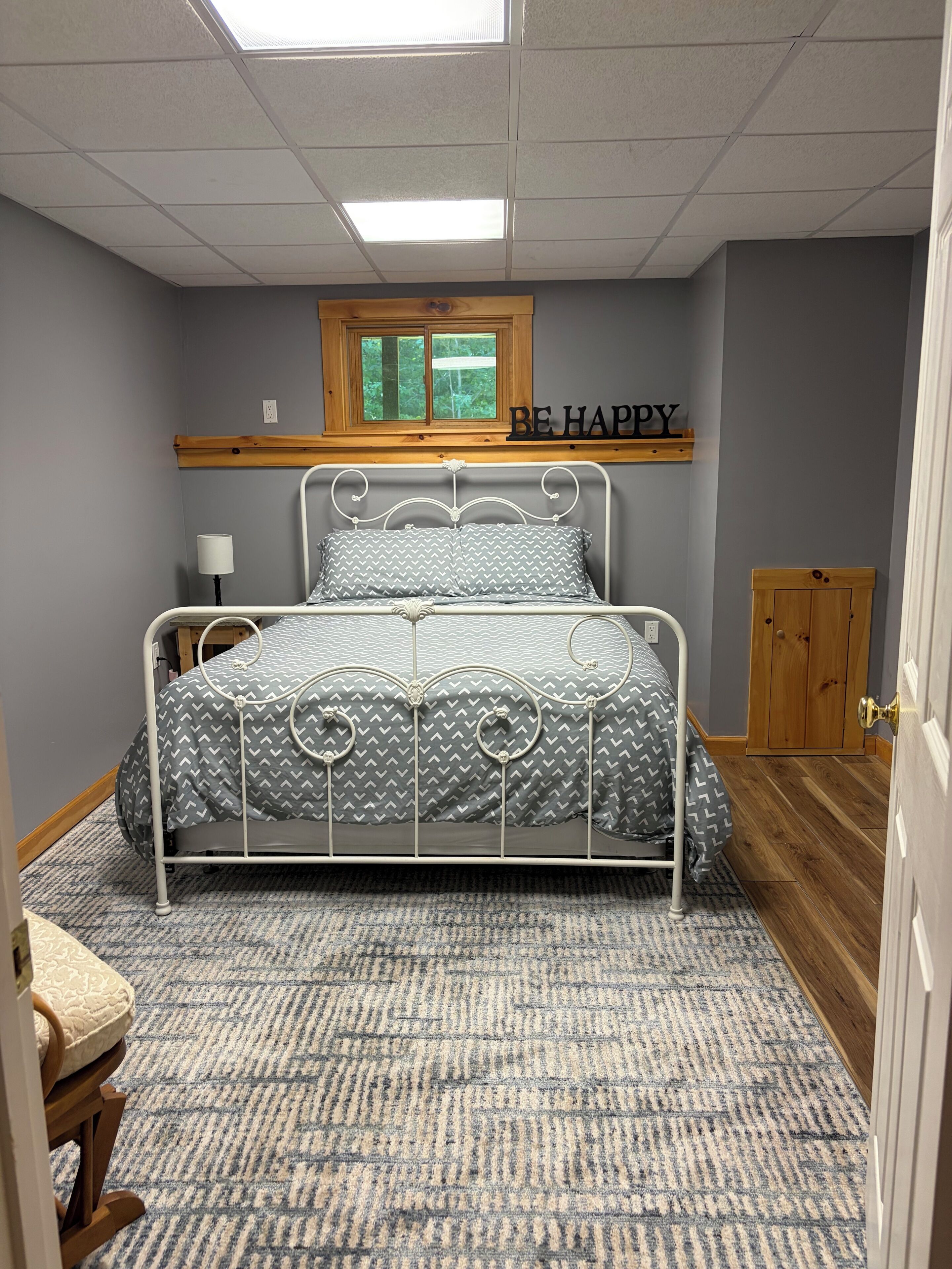Une chambre à coucher avec un lit, une fenêtre, une étagère fixée au mur avec une pancarte et une porte.