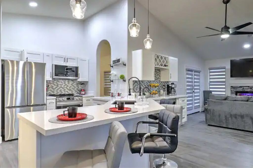 A modern kitchen with stainless steel appliances, a central island with seating, and a dining area with a sofa and chairs.