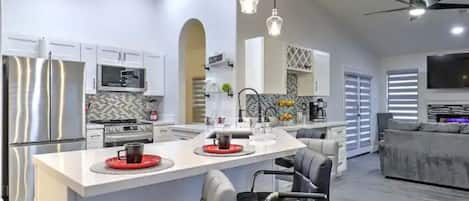 A modern kitchen with stainless steel appliances, a central island with seating, and a dining area with a sofa and chairs.