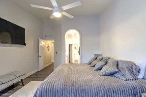 A bedroom with a bed, a ceiling fan, and a hallway leading to another room.