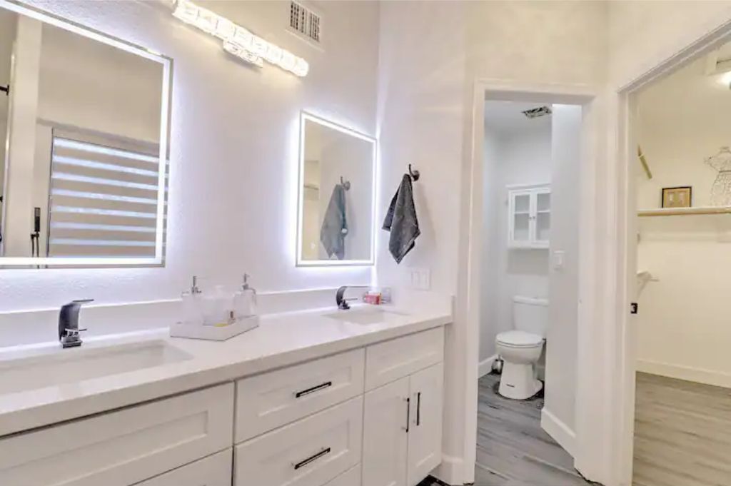 Een moderne badkamer met een wit wastafelmeubel, twee spiegels en een toilet.