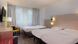 A hotel room with two beds, a desk, a chair, a TV, and a window with curtains. - Greet Berlin Alexanderplatz (Berlin)