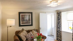 Een woonkamer met een bruine bank, gestreepte kussens, een houten salontafel met een bloevas, een vloerlamp en een ingelijst kunstwerk aan de muur.