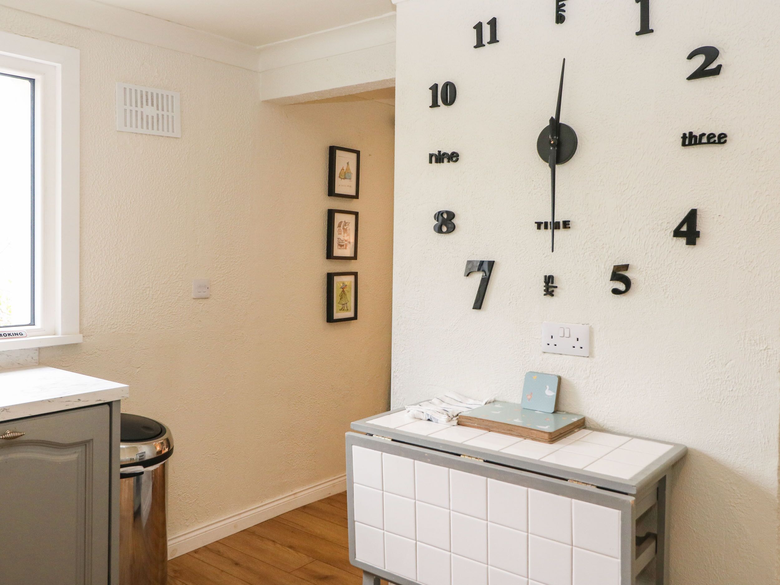 A room with a wall clock, a radiator, a window, and framed pictures.