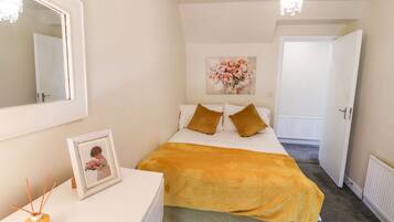 Une chambre à coucher comprenant un lit, une table de chevet, un miroir et une porte donnant sur une autre pièce.