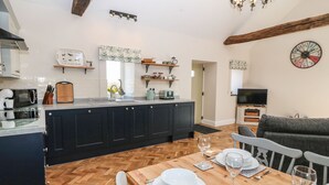 Una cocina moderna con armarios oscuros, una mesa de comedor de madera para cuatro comensales y un televisor en la sala de estar.