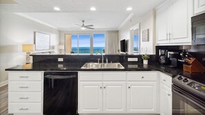 A modern kitchen with white cabinets, a black countertop, and a view of the ocean through large windows.
