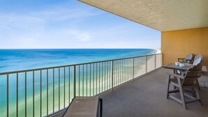 A balcony with a view of the ocean, a table with chairs, and a railing.