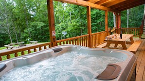 A wooden deck with a hot tub, picnic tables, and a bench overlooking a forest. - Hidden Creek Lodge by The Inn & Spa at Cedar Falls (Creola)