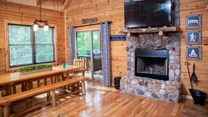 A wooden interior with a stone fireplace, a TV mounted above it, and a 'Welcome' sign. - Hidden Creek Lodge by The Inn & Spa at Cedar Falls (Creola)