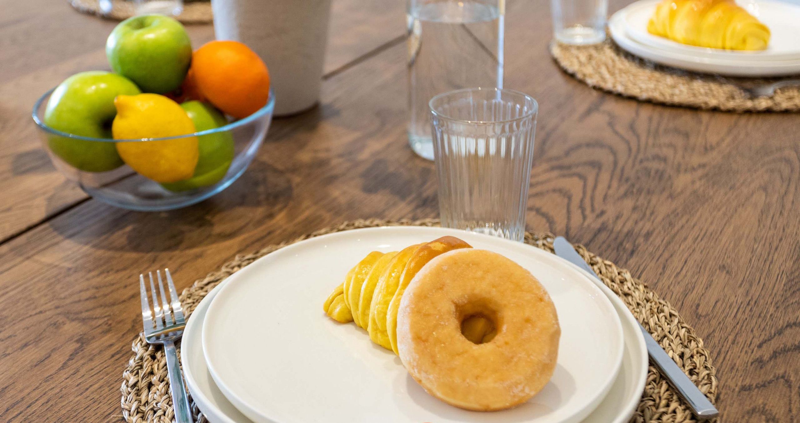 Una colazione: un piatto di cibo, una ciotola di frutta e un bicchiere d'acqua su un tavolo di legno.