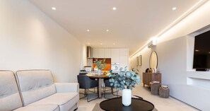 Un salon moderne avec un canapé, une table à manger et des chaises, une table basse avec un vase, et une cuisine en arrière-plan.