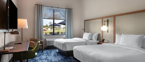 Ett hotellrum med två sängar, ett skrivbord, en stol, en TV och ett fönster med utsikt över omgivningen.