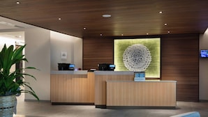 A modern reception area with wooden reception desks, a large decorative wall piece, and a television mounted on the wall. - Fairfield Inn & Suites By Marriott Coastal Carolina Conway (Conway)