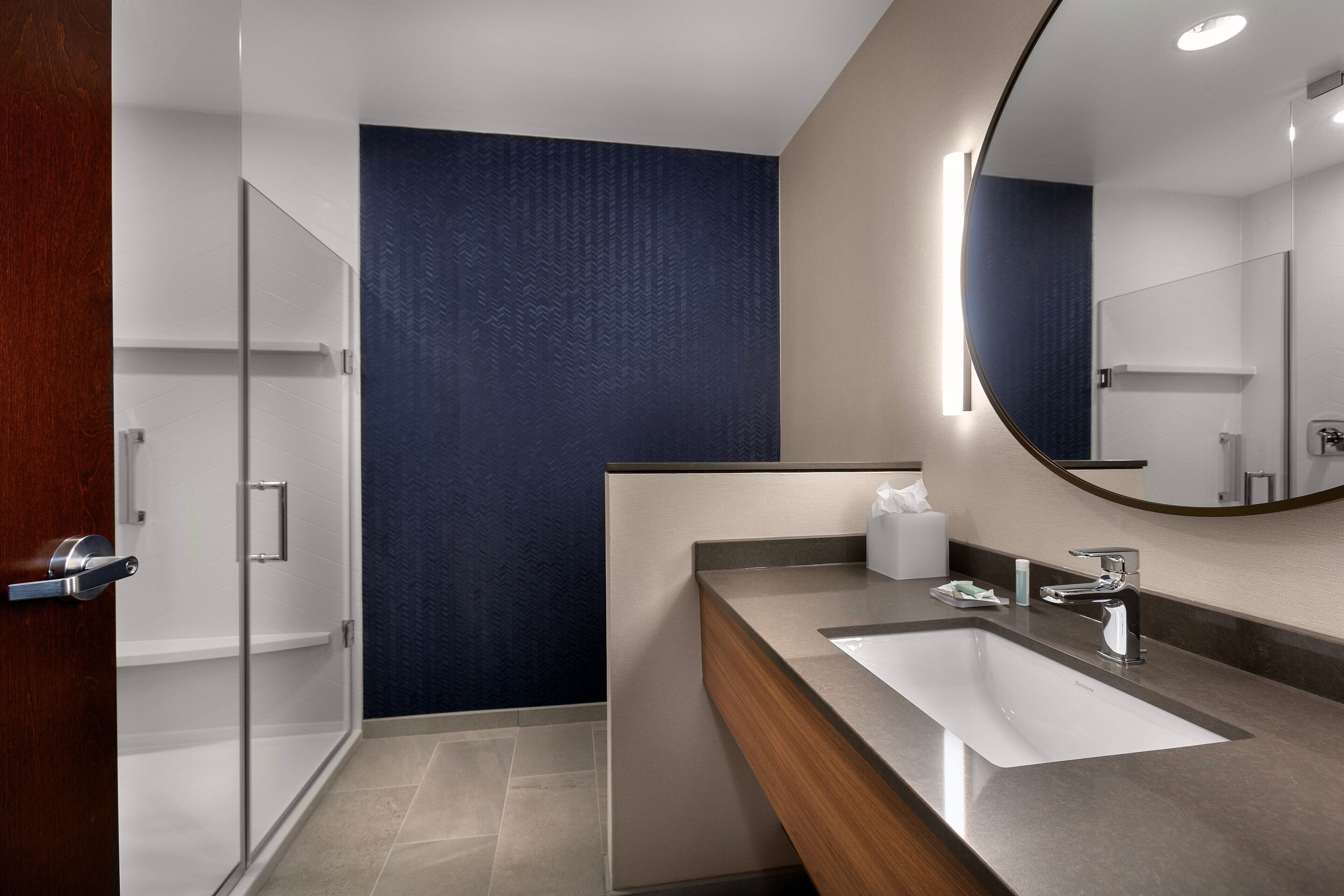 A modern bathroom with a large mirror, a sink, and a shower area.