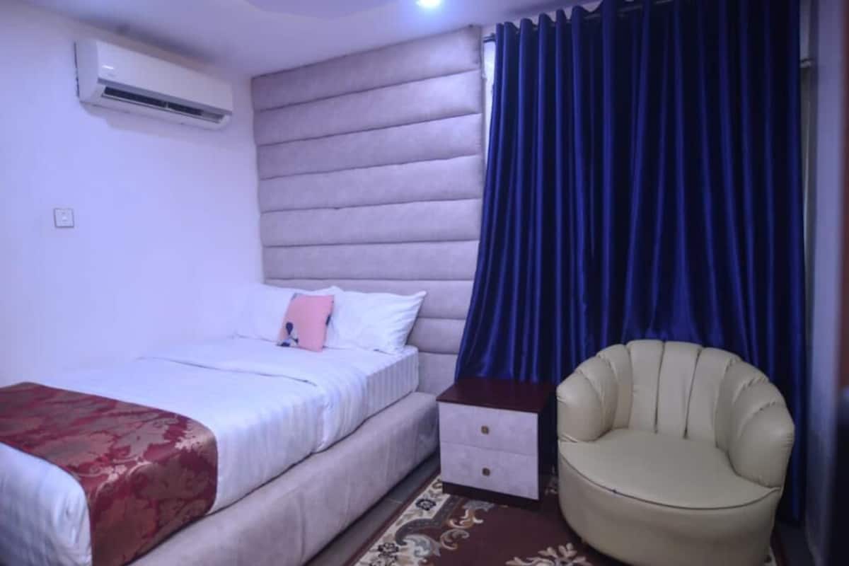 A bedroom with a bed, a nightstand, a chair, and a blue curtain.