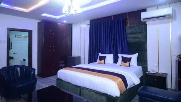 A modern hotel room with a large bed, dark curtains, and a chandelier. - Nobi's Apartments (Lagos)