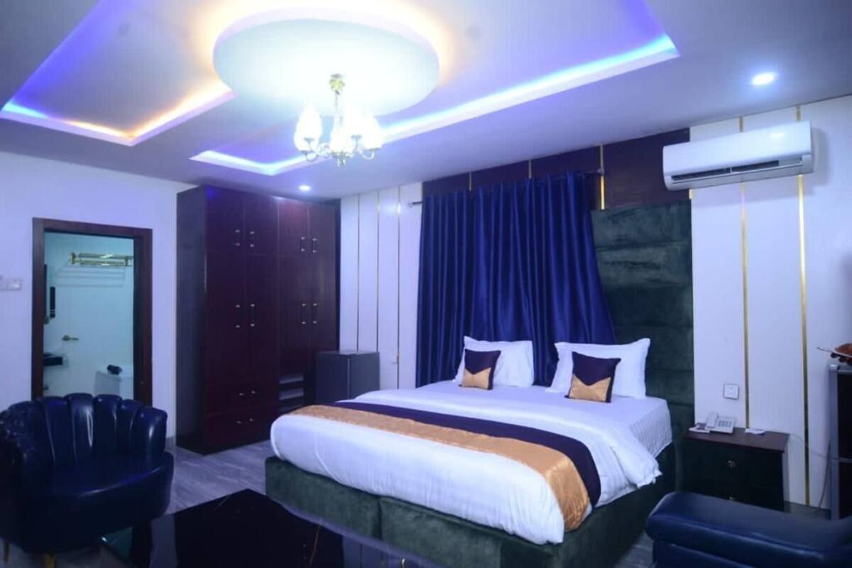 A modern hotel room with a large bed, dark curtains, and a chandelier.