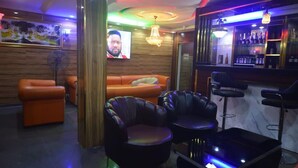 A bar area with leather seating, a television, and a bar stocked with bottles. - Nobi's Apartments (Lagos)