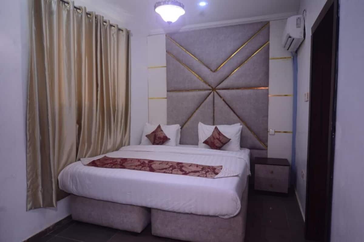 A neatly arranged bedroom with a bed, curtains, a headboard with a geometric pattern, and a bedside table.