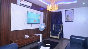 A modern living room with a flat-screen TV, a fan, a chandelier, and a blue leather sofa. - Nobi's Apartments (Lagos)