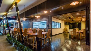 An indoor dining area with wooden tables and chairs, pendant lighting, and a view of the kitchen through a large window. - The Landmark Patong (Patong)