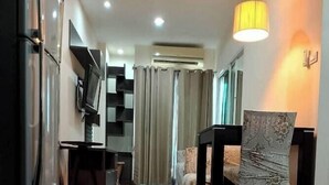 A modern living room with a wooden floor, a dining area with a table and chairs, a TV, and an air conditioning unit. - The Landmark Patong (Patong)