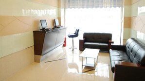A modern hotel lobby with a reception desk, a black leather sofa, a small table, and a large window with curtains. - Hong Kong Cosco Hotel (Hong Kong)