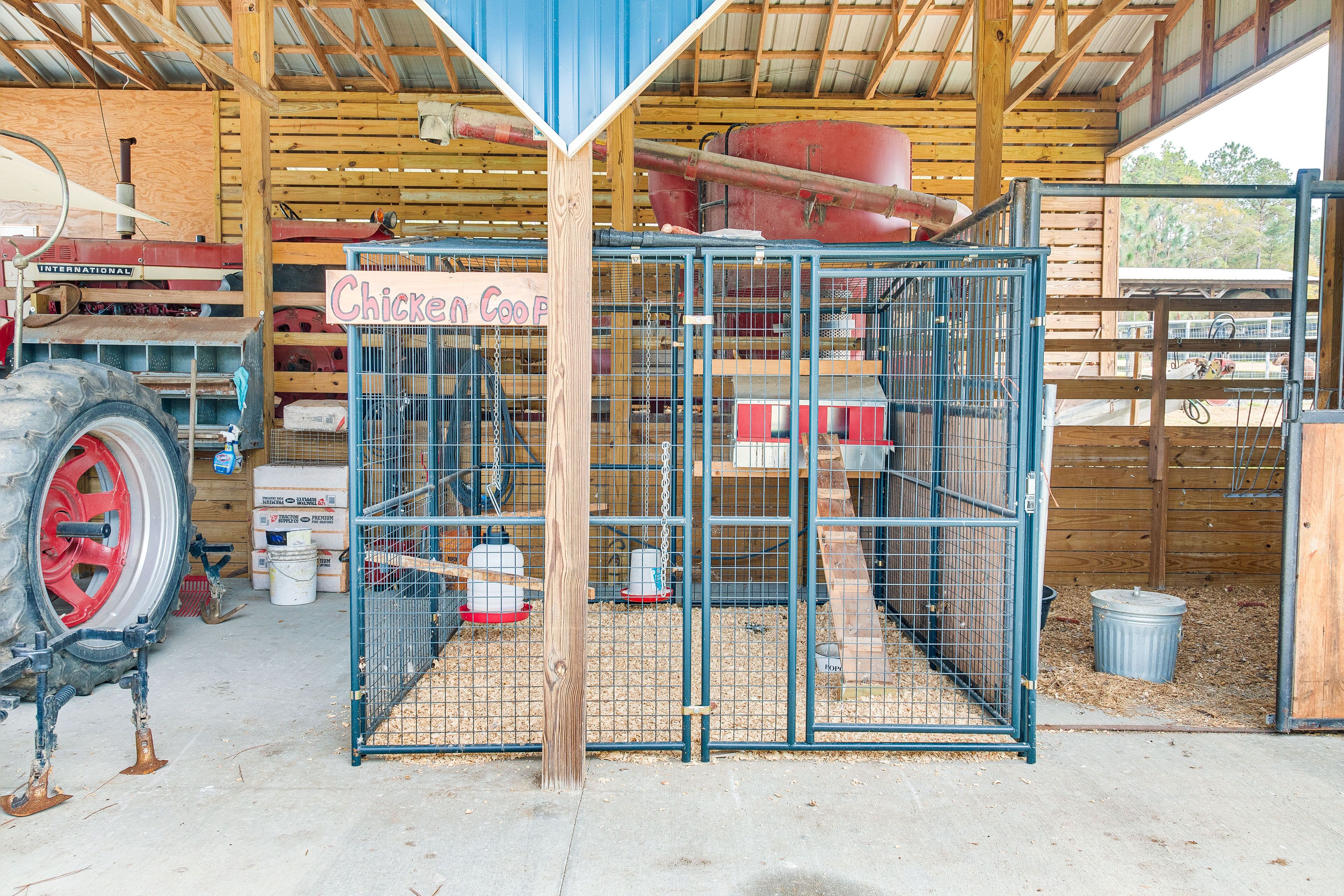 A chicken coop with a wooden sign, surrounded by farm equipment and supplies.