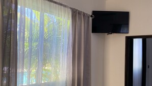 Quarto com uma janela grande coberta por cortinas finas, uma televisão de tela plana na parede e uma escada visível que leva a outro andar.