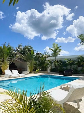 A swimming pool with lounge chairs, surrounded by tropical plants and a clear blue sky. - The White Rock Hotel BB (Guayacanes)
