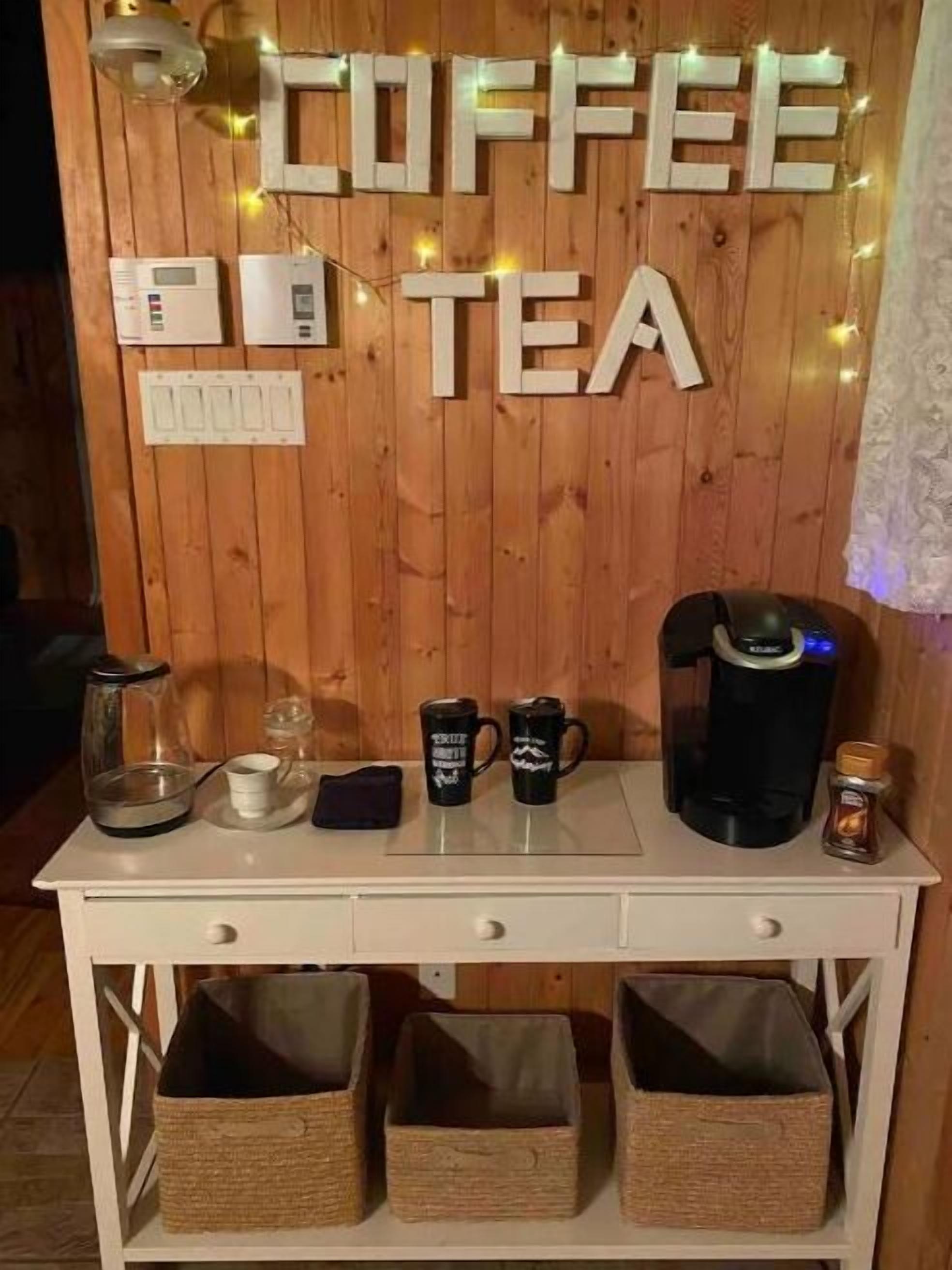 A coffee and tea station with a wooden backdrop, a coffee maker, two mugs, a teapot, and a kettle.