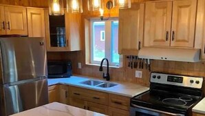 A modern kitchen with wooden cabinets, a stainless steel refrigerator, a black stove, and a marble countertop. - Cottage by River Falls with Hot Tub & Sauna (Amherst)
