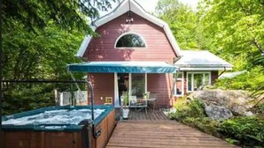 A wooden deck leading to a red house with a covered porch and a hot tub. - Cottage by River Falls with Hot Tub & Sauna (Amherst)