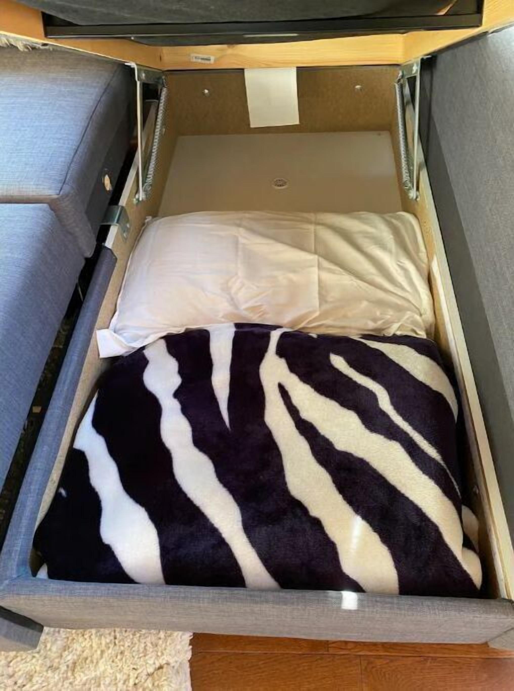 A compact bed with a zebra-patterned blanket and a white pillow in a small, enclosed space with a wooden frame and a beige carpet.