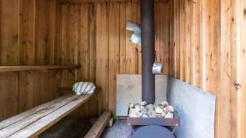 A wooden sauna room with a bench, a wood-burning stove, and a bench with a pillow.