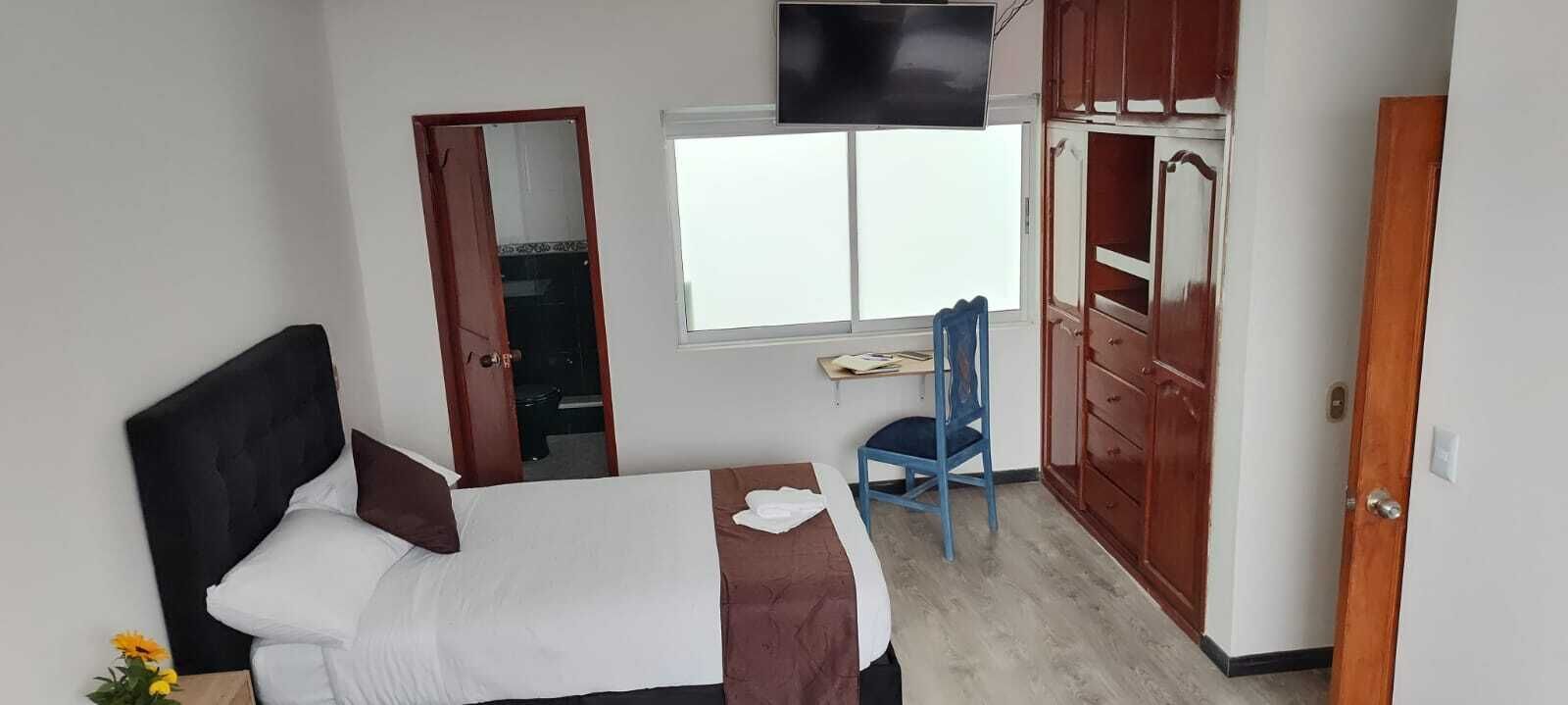 Un dormitorio con cama, televisor en la pared, ventana y armario.