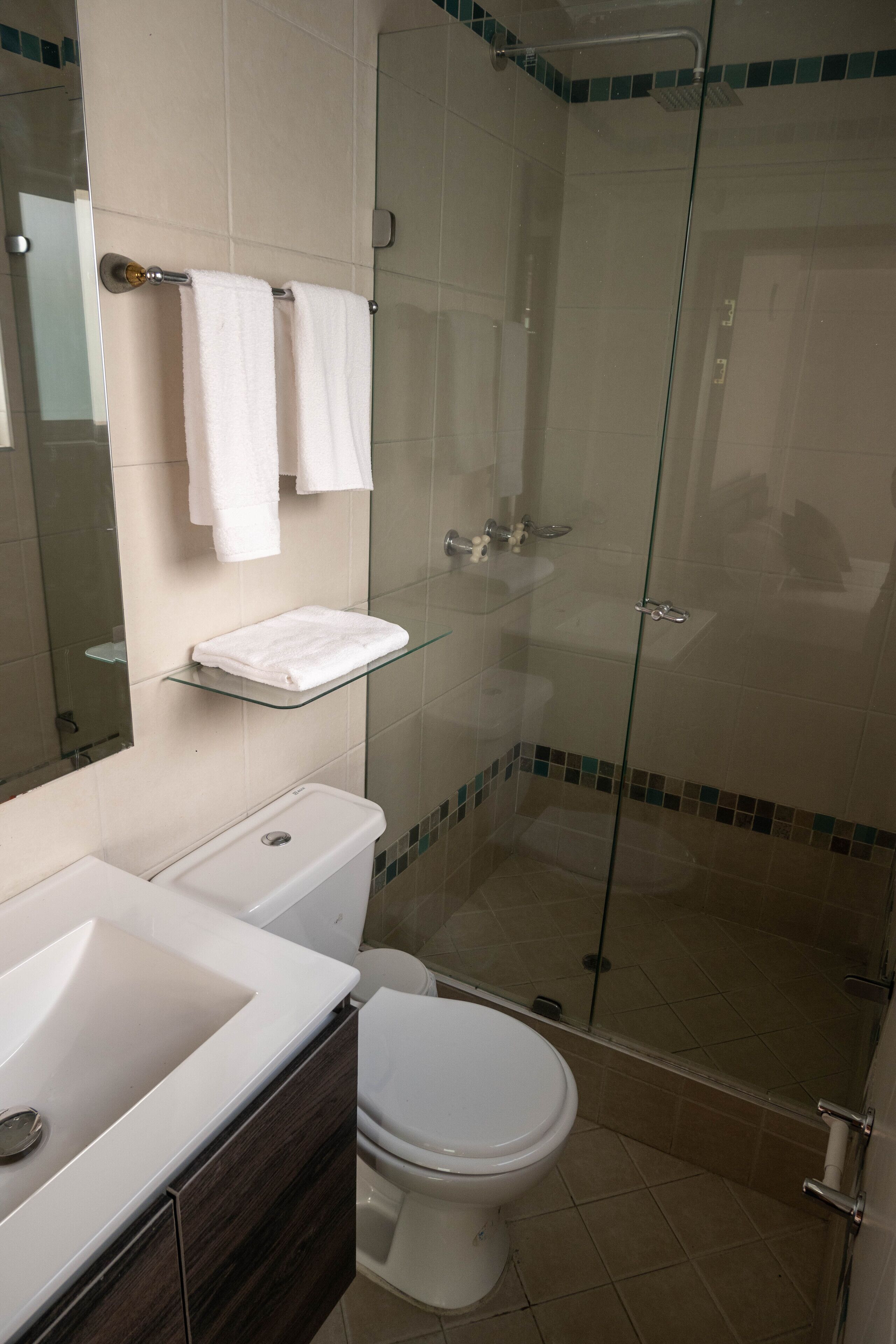 Un bany amb dutxa d'acer, un vàter blanc, un lavabo i un mirall.