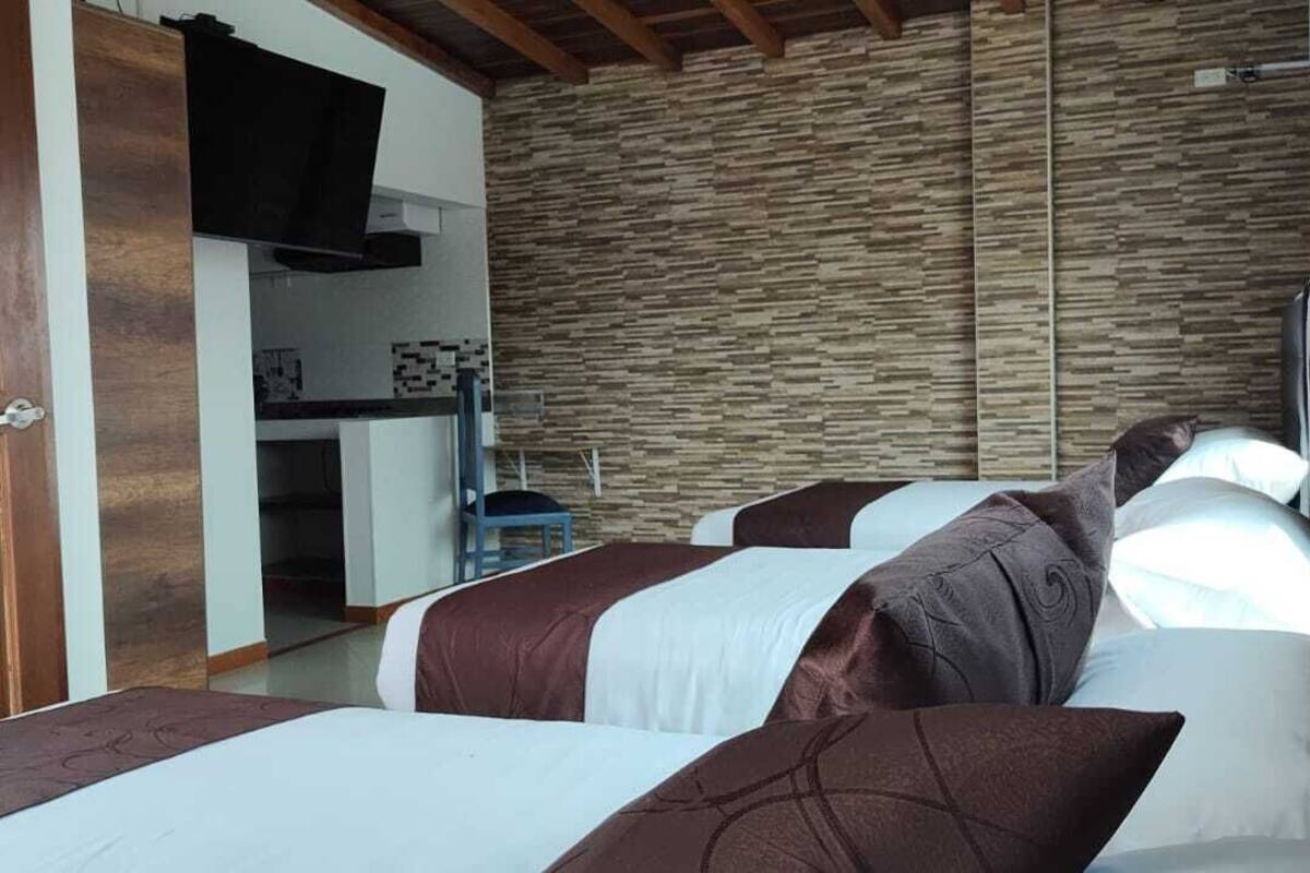 A bedroom with a stone wall, a TV, and a bed with multiple pillows.