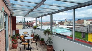 Une terrasse couverte avec un toit en verre, des plantes en pot et des meubles d’extérieur.