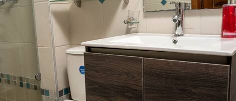 A bathroom with a white toilet, a wooden cabinet, a glass shelf, and a mirror above the sink.