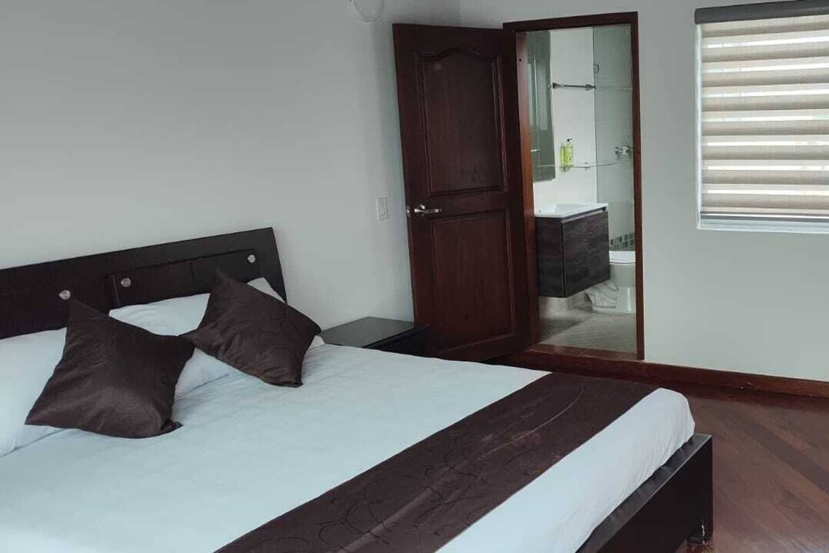 A bedroom with a bed, a nightstand, a chair, a wardrobe, and a window with blinds.
