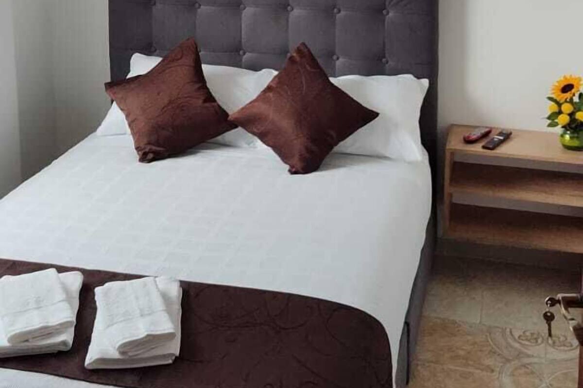 A neatly made bed with a dark headboard, white and brown bedding, and two folded towels on the side.