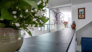 Un intérieur moderne avec une table en bois, une plante en pot aux fleurs blanches, une chaise bleue et une enseigne indiquant « La Nona CASA BOUTIQUE ».