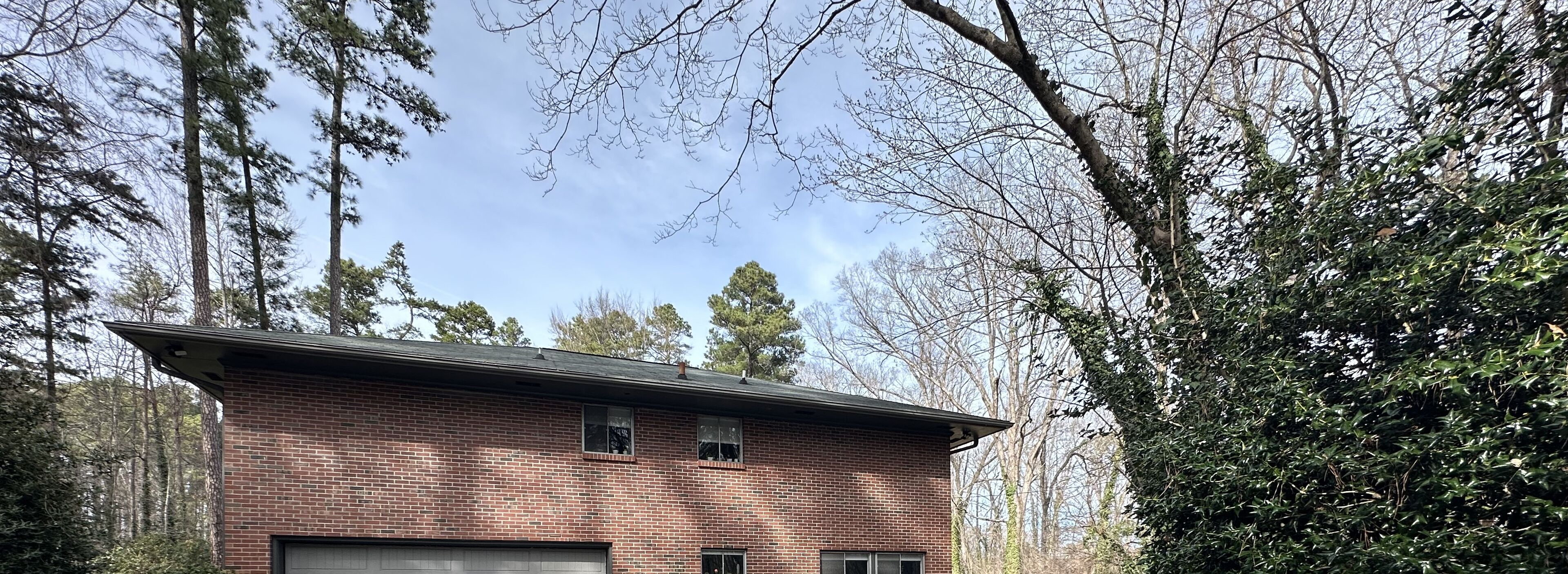 A two-story brick house with a garage, surrounded by trees and a clear sky.