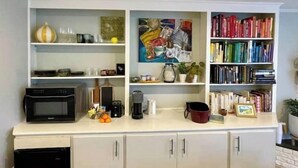 A kitchen with a microwave, coffee maker, and various kitchen items on the counter. There are cabinets below and a bookshelf filled with books to the right. - Guest Suite near UNC! (Chapel Hill)