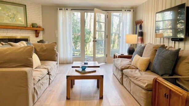 A living room with two beige sofas, a wooden coffee table, and a TV mounted on the wall. - Guest Suite near UNC! (Chapel Hill)