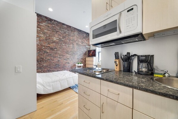 A compact kitchen with a brick wall, a microwave, a coffee maker, and a sink.