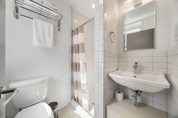 A modern bathroom with a toilet, shower, sink, and a mirror.