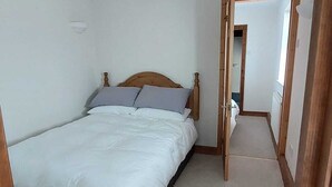 Ein Schlafzimmer mit einem Bett, einem Holz-Kopfstück, einer Deckenleuchte und einer Tür zu einem anderen Raum.